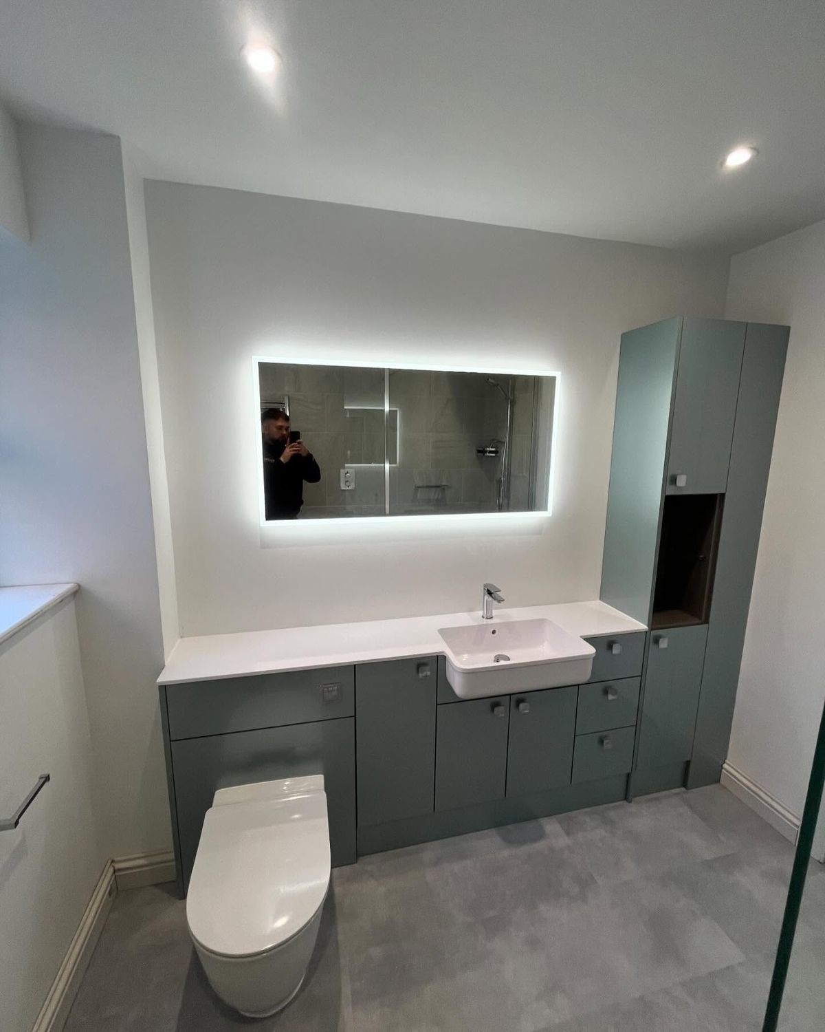 Bathroom with sage green fitted units and a backlit mirror