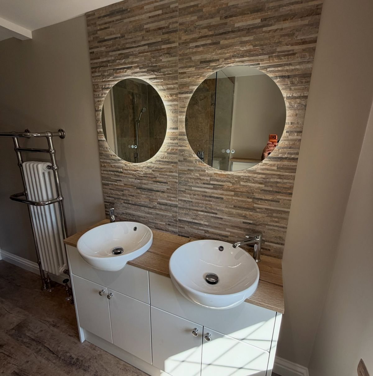 Bathroom with a stone-effect feature wall, two backlit round mirrors and twin basins