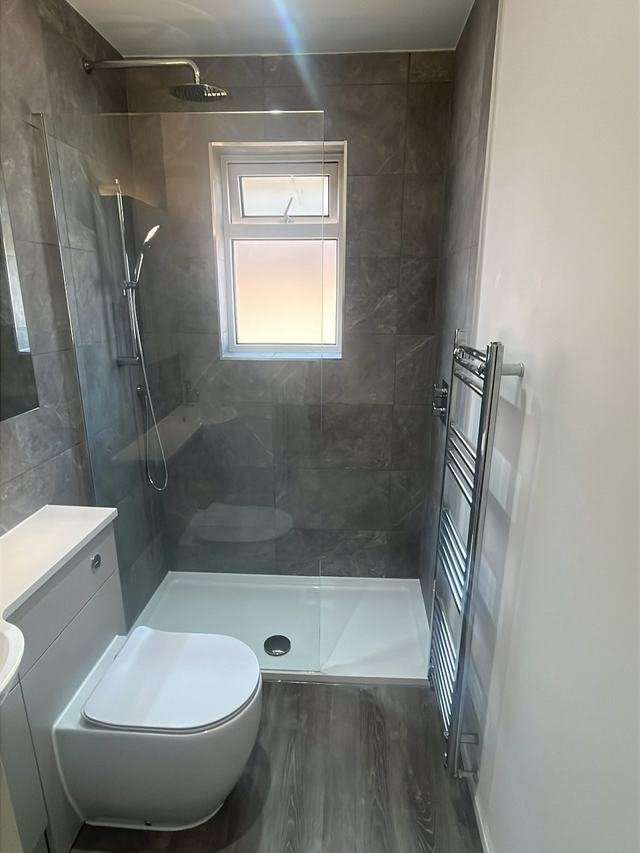 Grey tiled en suite with a walk-in shower and a tall chrome towel rail