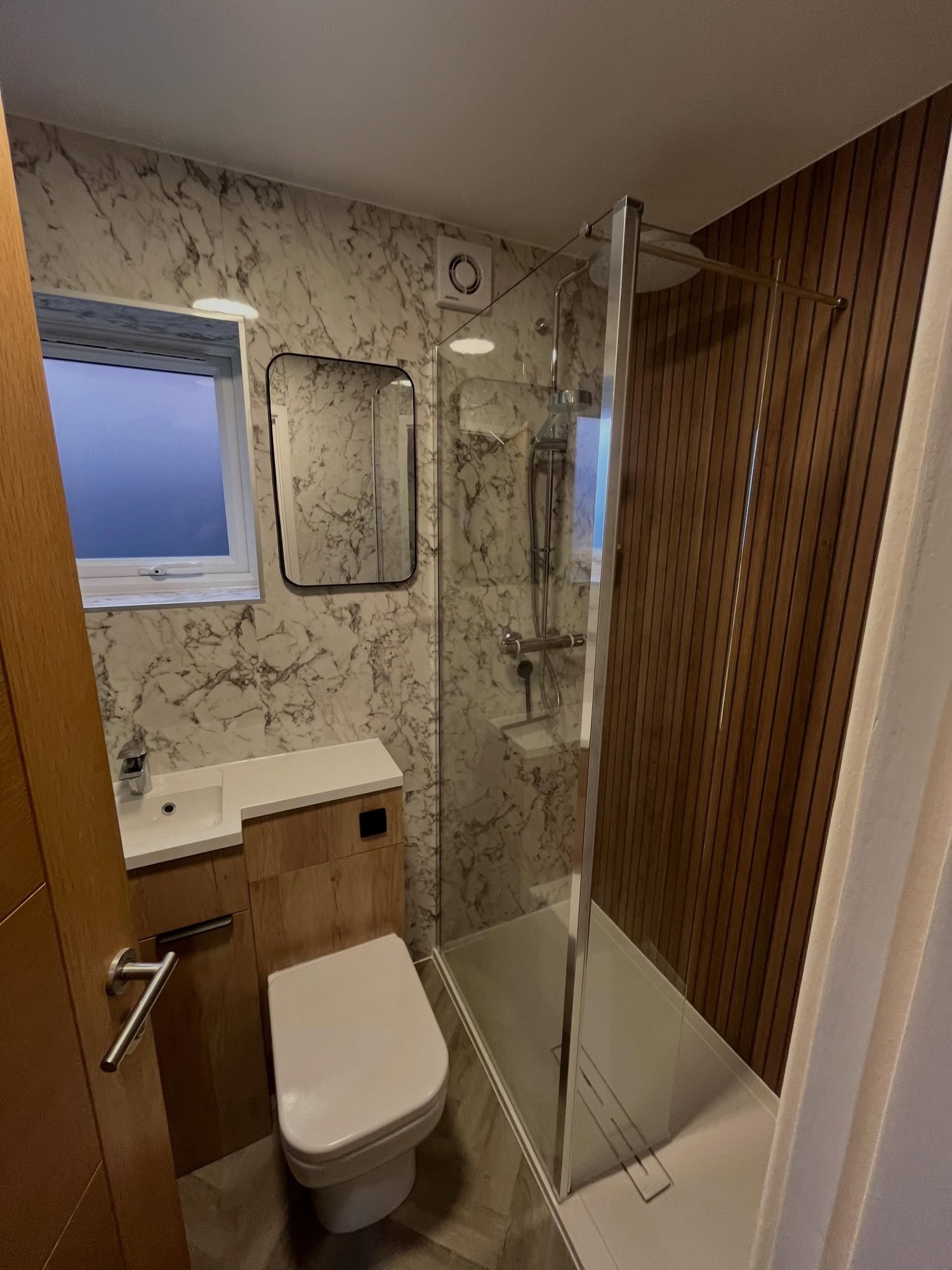 Shower room with marble-effect walls, a timber slatted panel and a glass screen