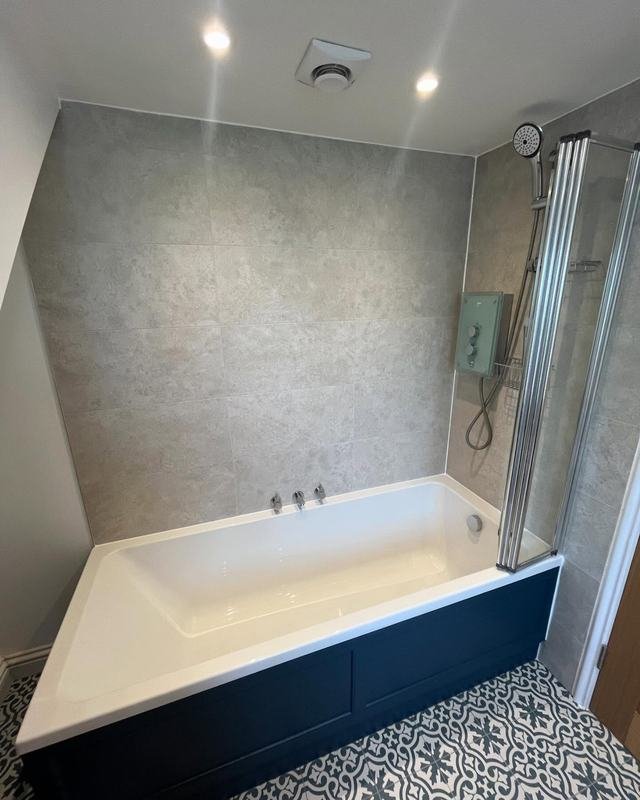 Loft conversion en suite with a bath, shower screen and patterned floor tiles