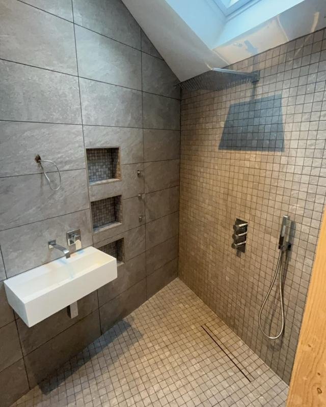Walk-in shower with large grey tiles, mosaic tiles and two recessed niches